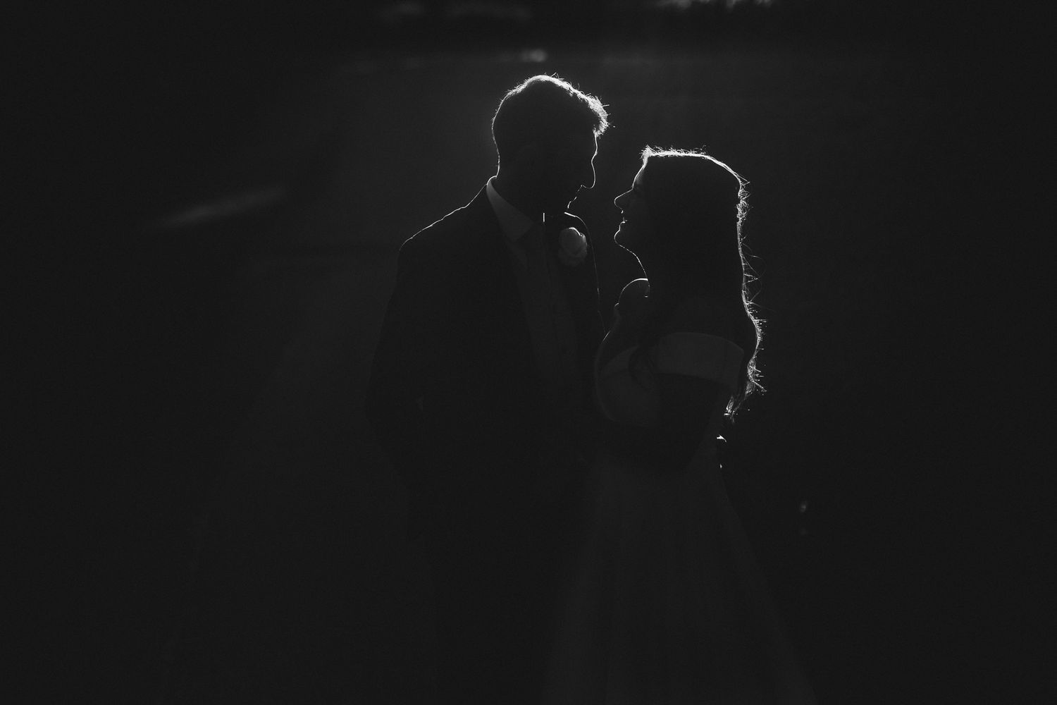 A romantic silhouette of a couple embracing in dramatic backlit black and white photography.