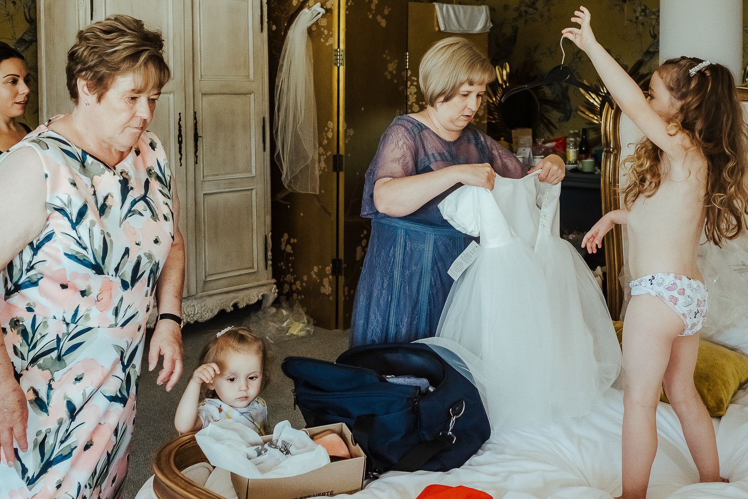 Group getting ready in a dressing room with wedding dress and baby in high chair.