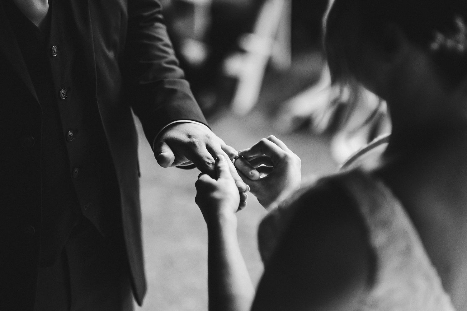 Close-up detail shot of hands exchanging wedding rings during ceremony.