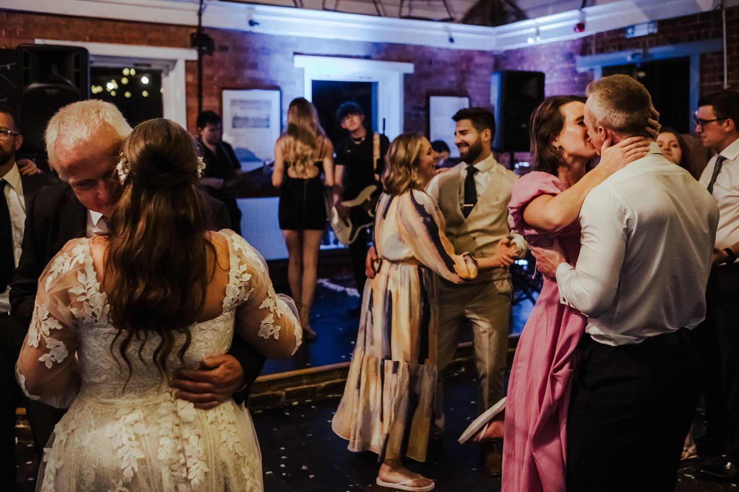 Wedding reception guests dancing and celebrating in a venue with blue mood lighting.