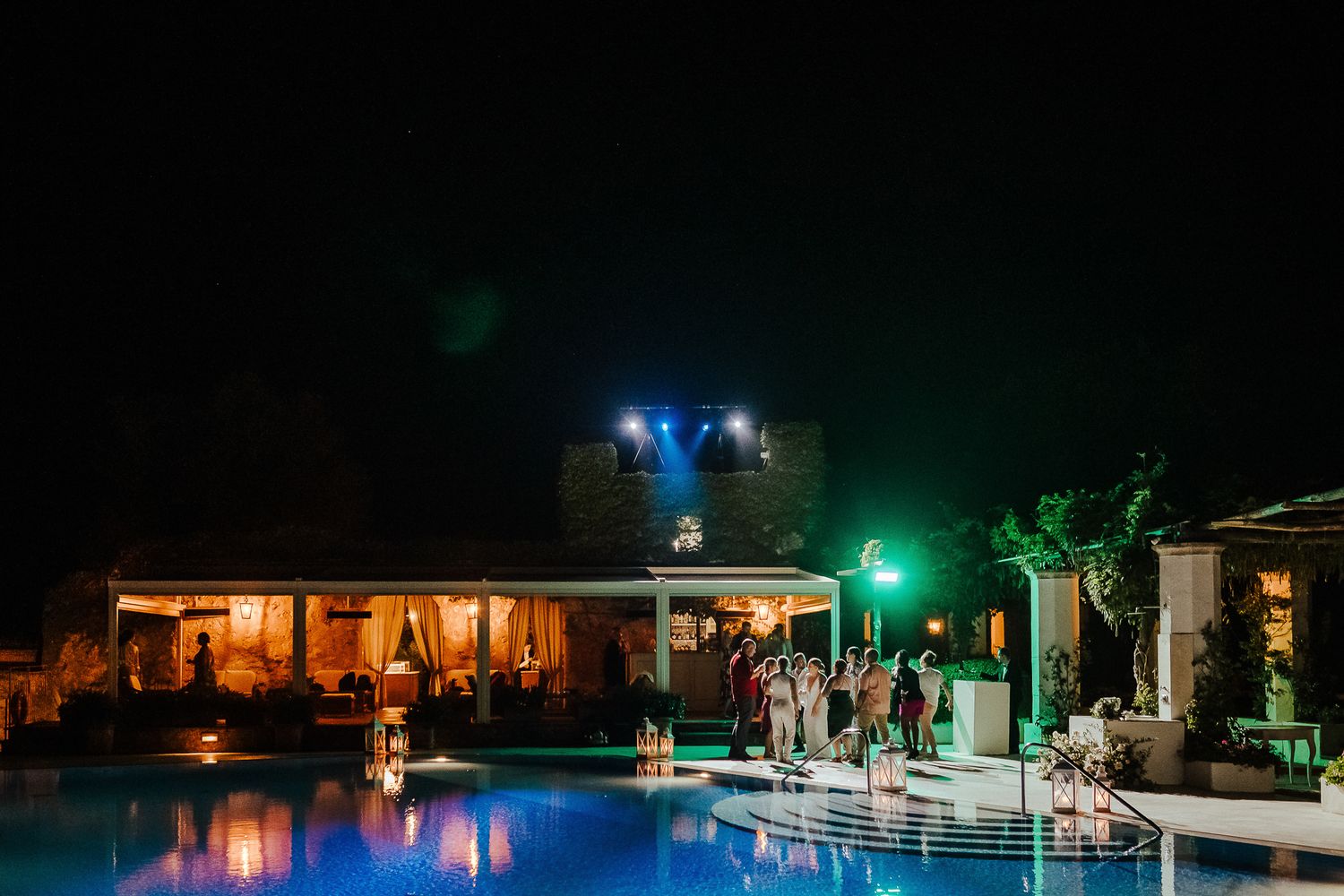 Nighttime wedding reception by illuminated pool with atmospheric lighting and decor.
