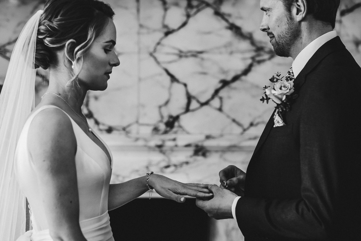 Intimate moment of ring exchange during wedding ceremony in black and white.