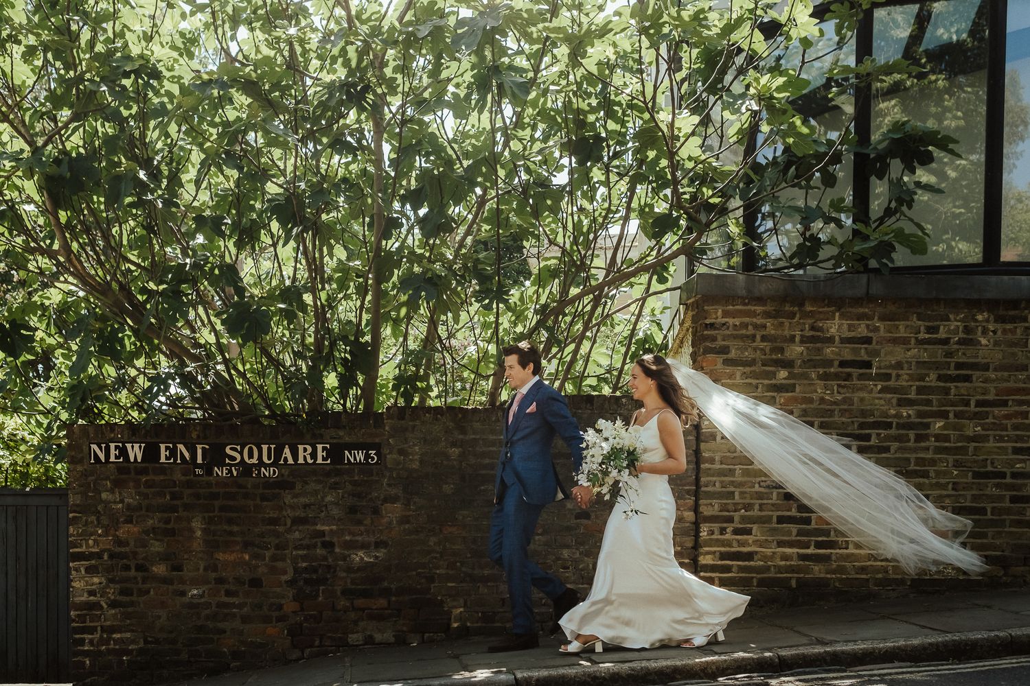 A wedding couple poses playfully against a brick wall at New Inn Square.
