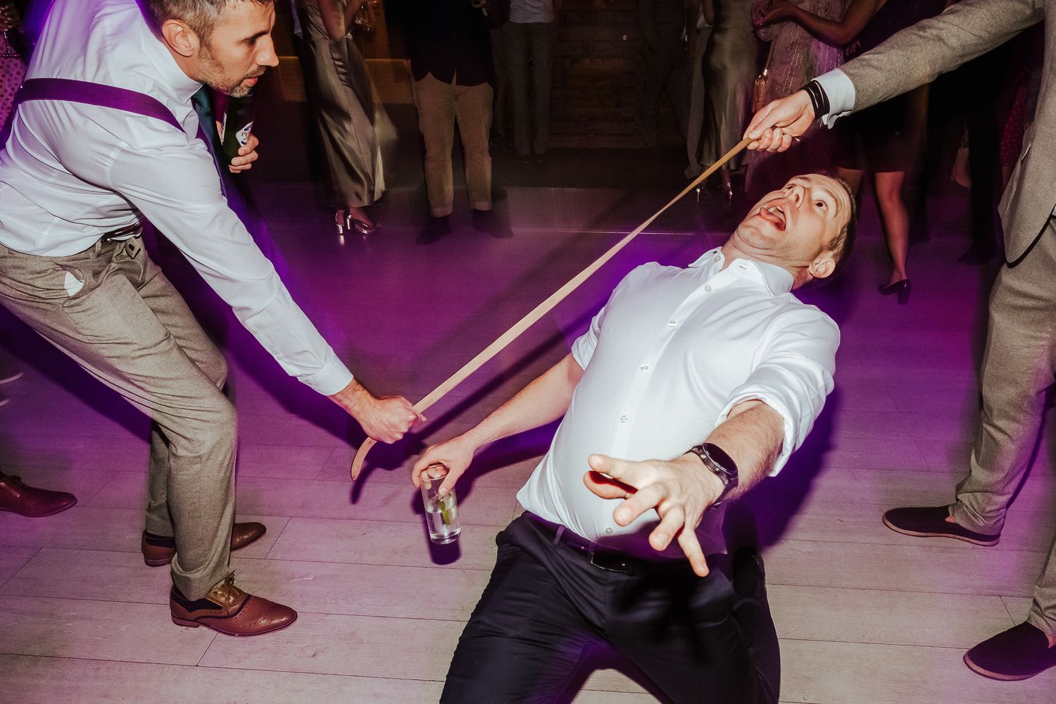 Party guest leans back dramatically during limbo dance under purple lighting.