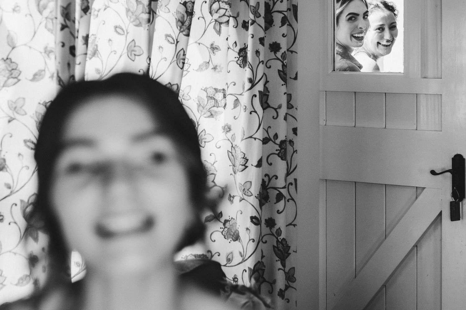 Blurred artistic black and white portrait through floral curtains in a rustic room.