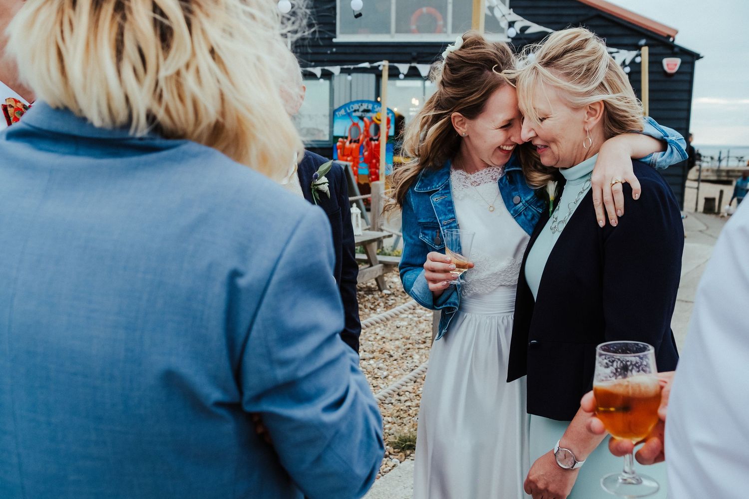 Friends share laughter and drinks during an outdoor wedding celebration.