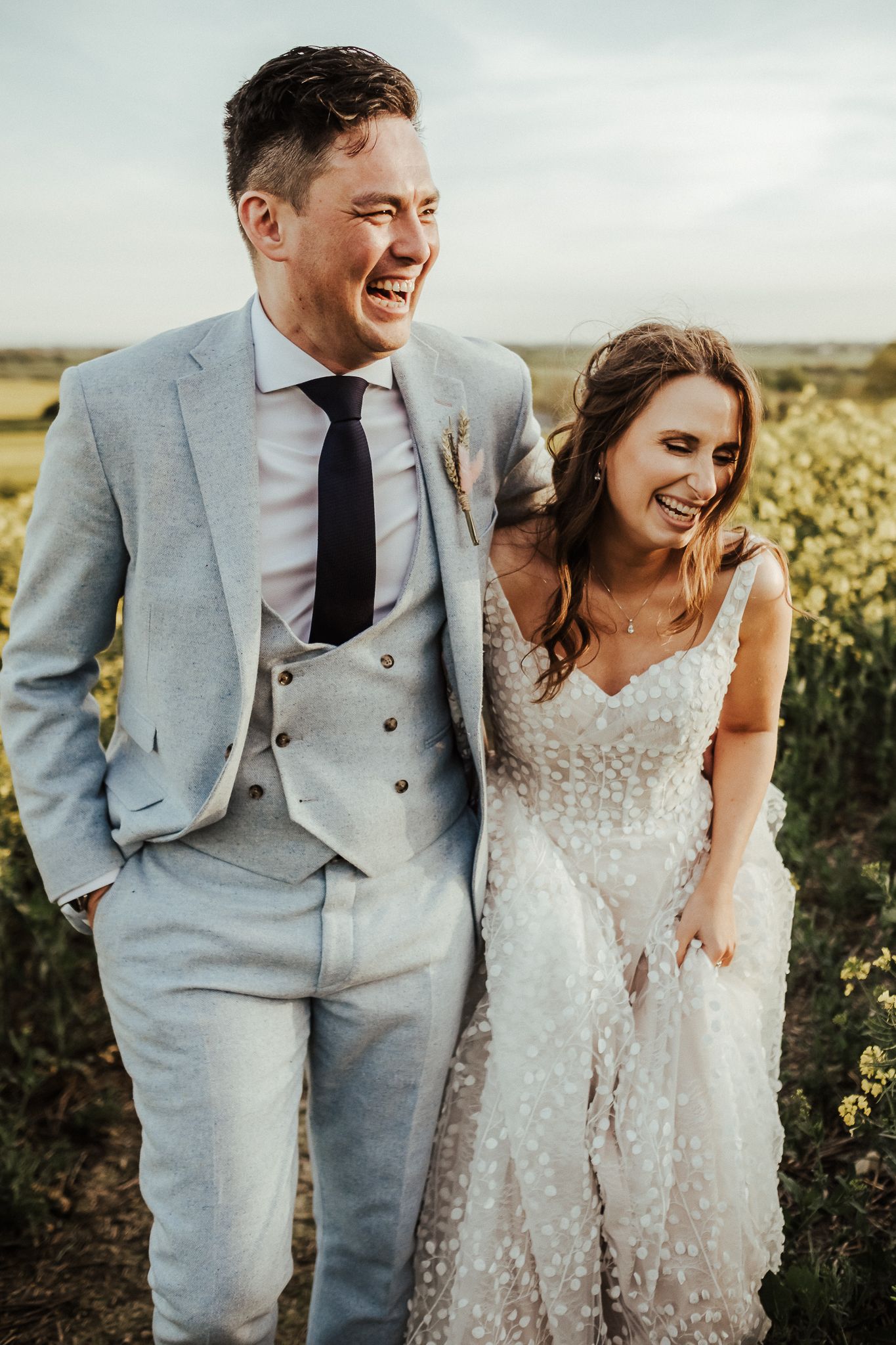 Joyful couple sharing a laugh in countryside setting wearing wedding attire.