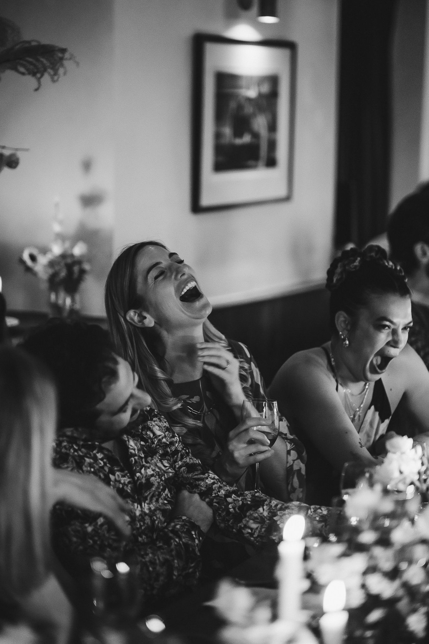 Black and white candid photo of people laughing together at a dinner party with glowing candles in the foreground.