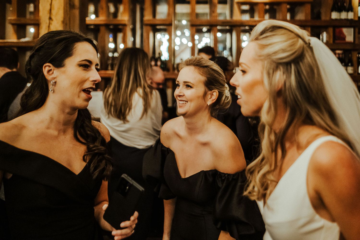Bridesmaids in black dresses share joyful moment at wedding celebration.