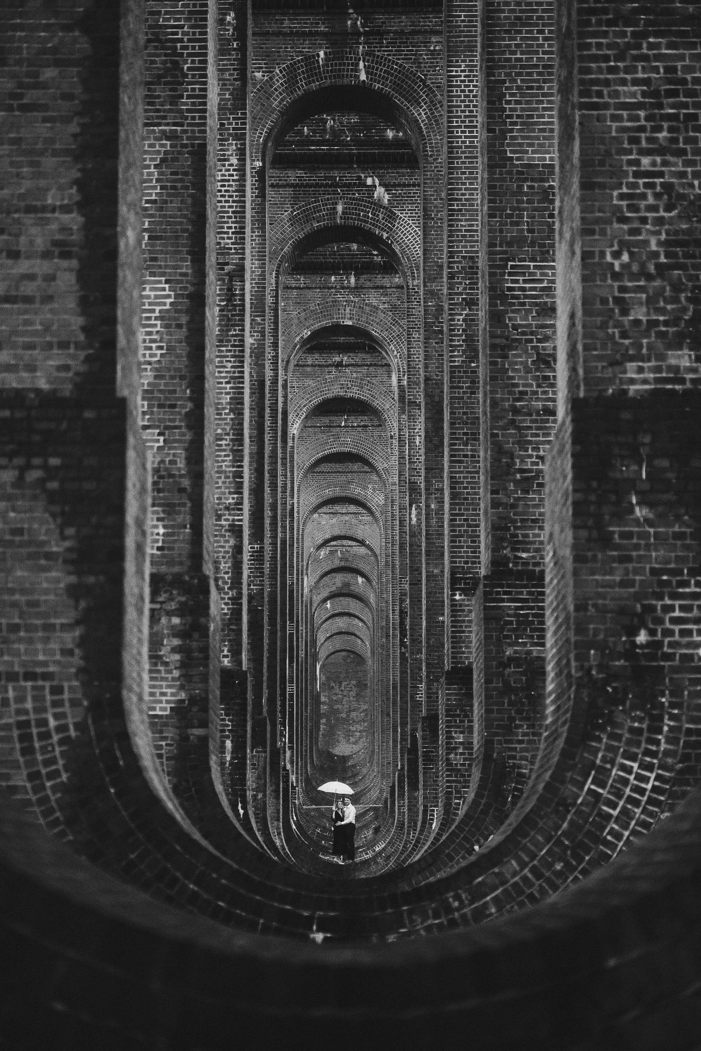 Dramatic black and white perspective through a series of brick arched viaducts creating a tunnel-like effect.