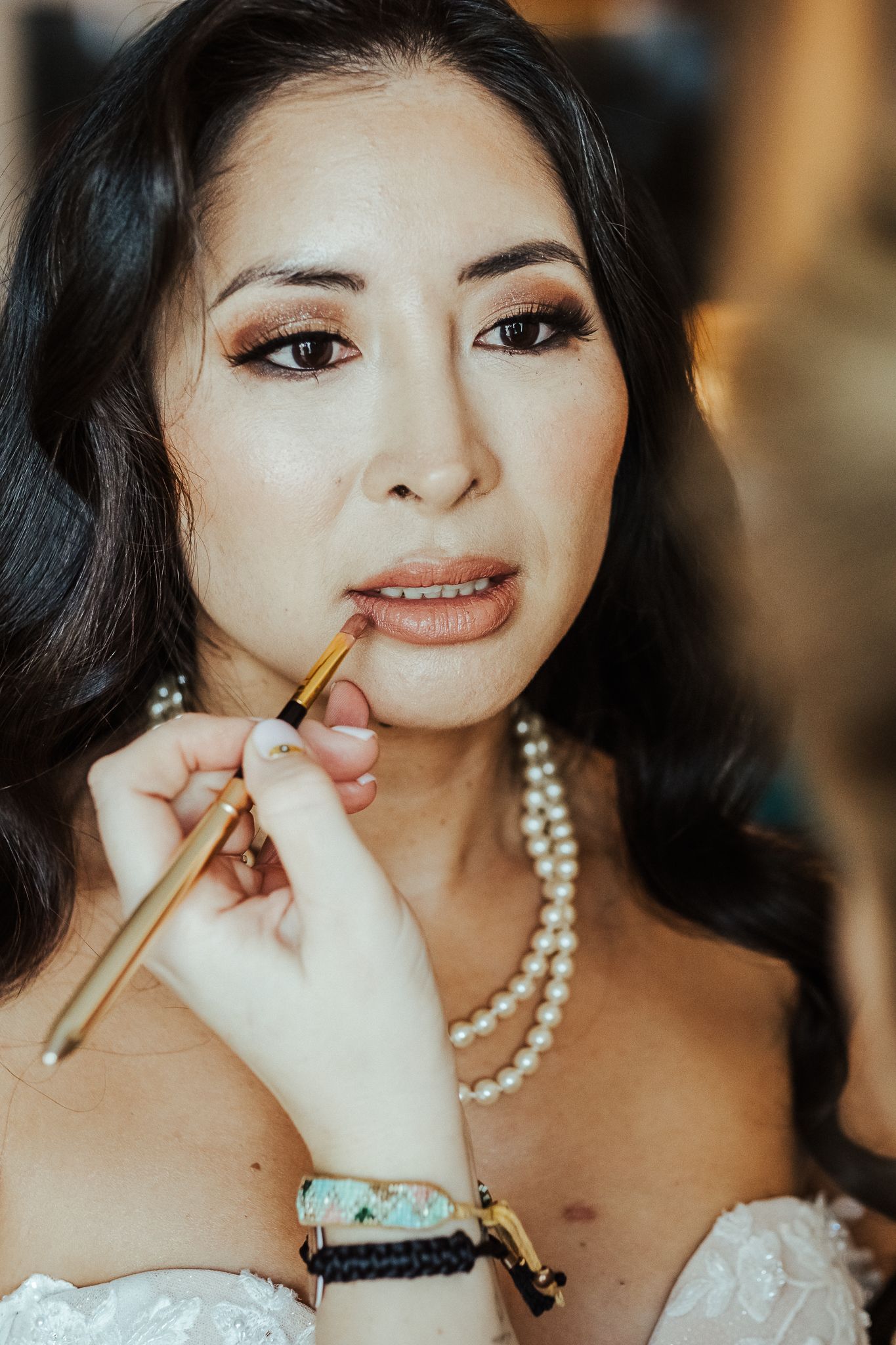 Close up shot of final touches being applied to bridal makeup with pearl necklace.
