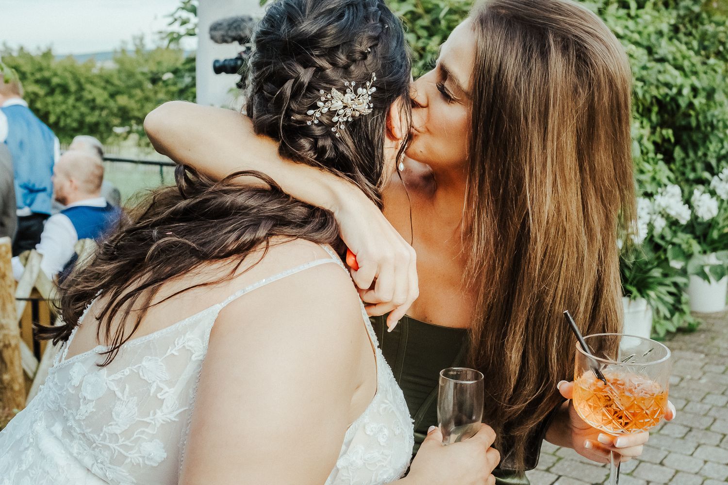 Two guests share an affectionate moment during an outdoor wedding reception with drinks.