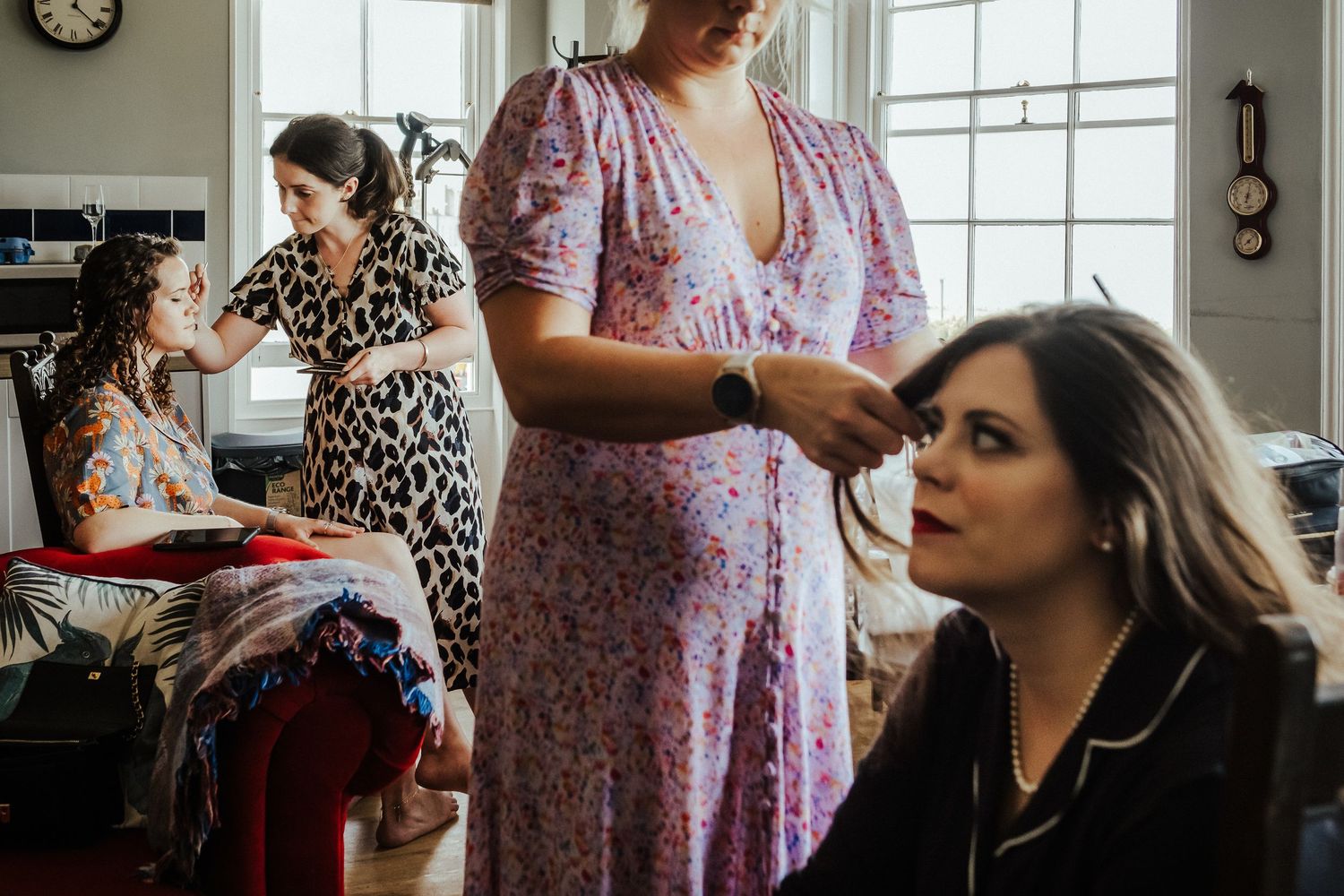 Wedding preparations show people getting ready in a sunlit room with floral dresses and makeup being applied.