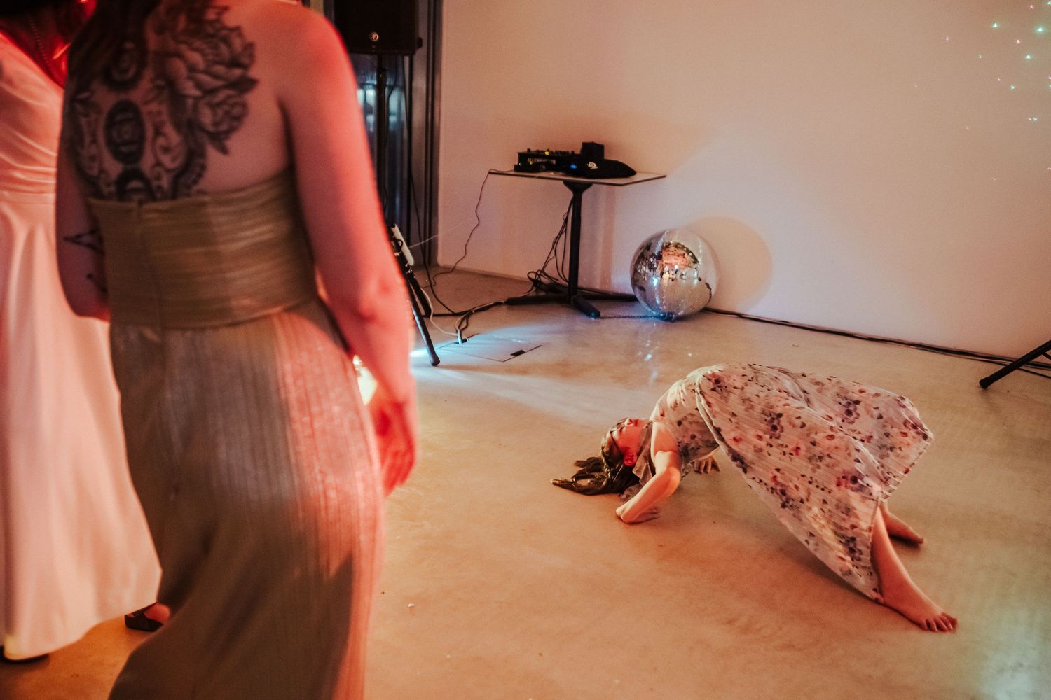 Person in floral dress lies on dance floor during party with red ambient lighting.