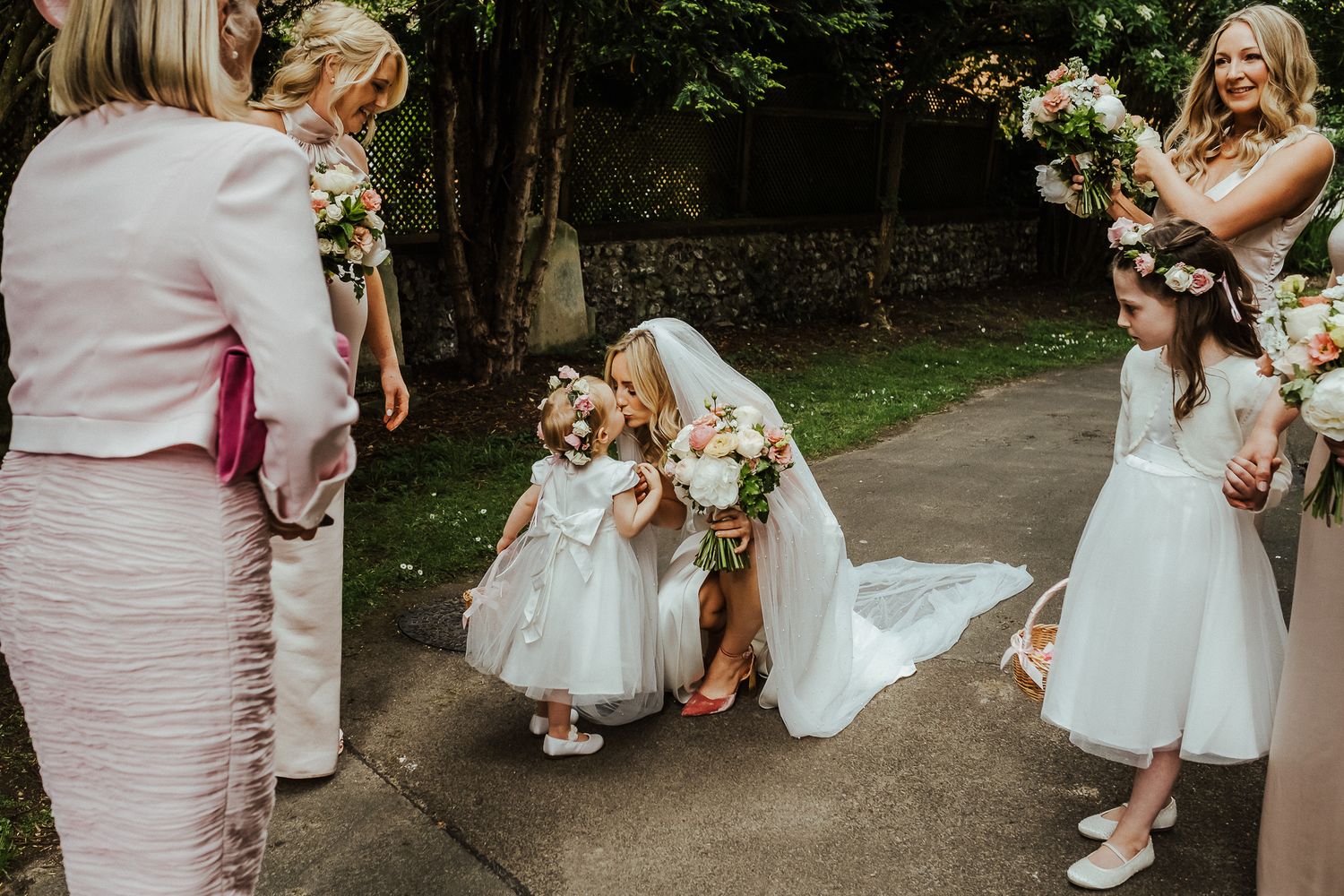 Wedding party members pose with colorful floral arrangements in an outdoor garden setting.