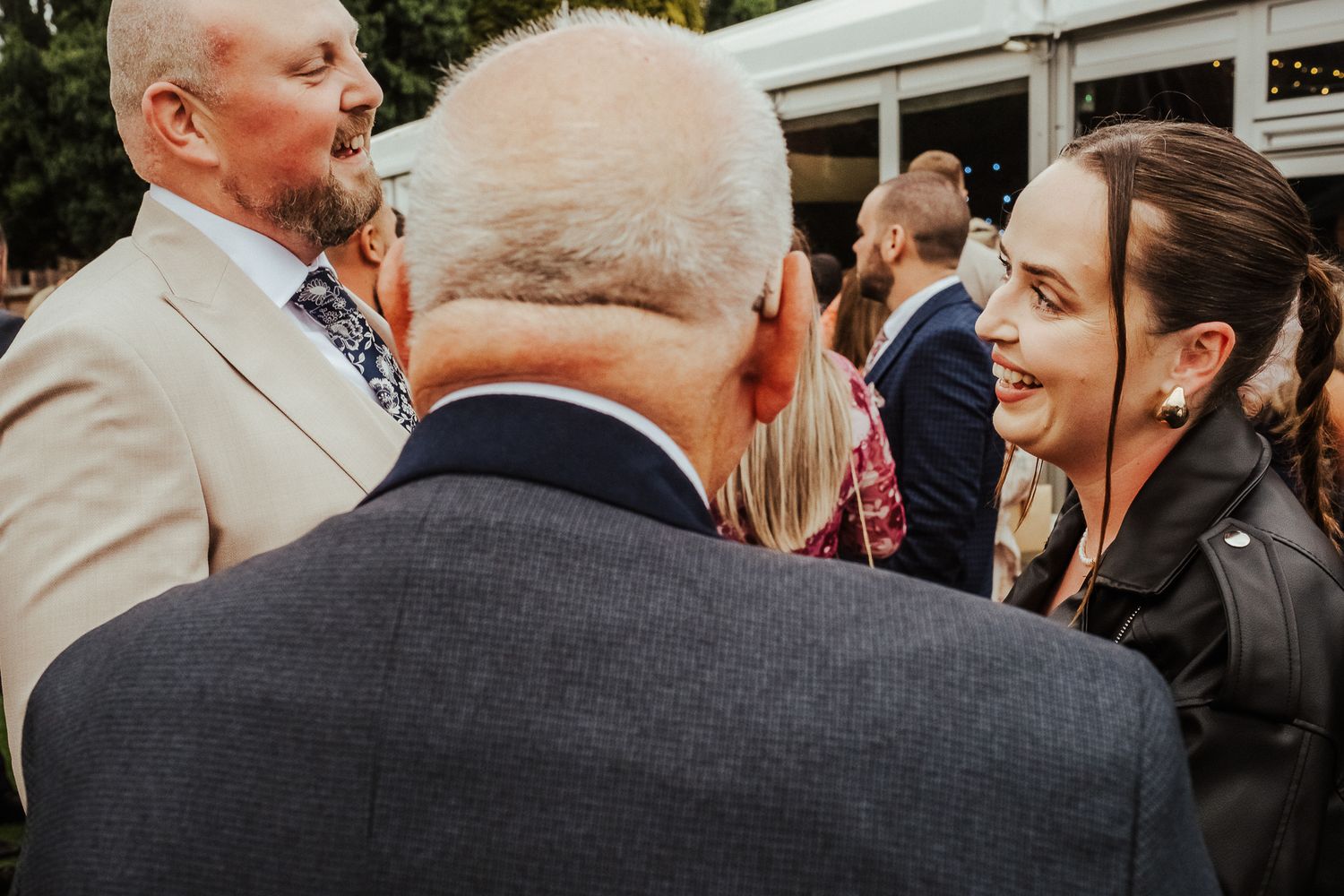 Candid black and white photo captures laughter and celebration at an outdoor wedding reception.