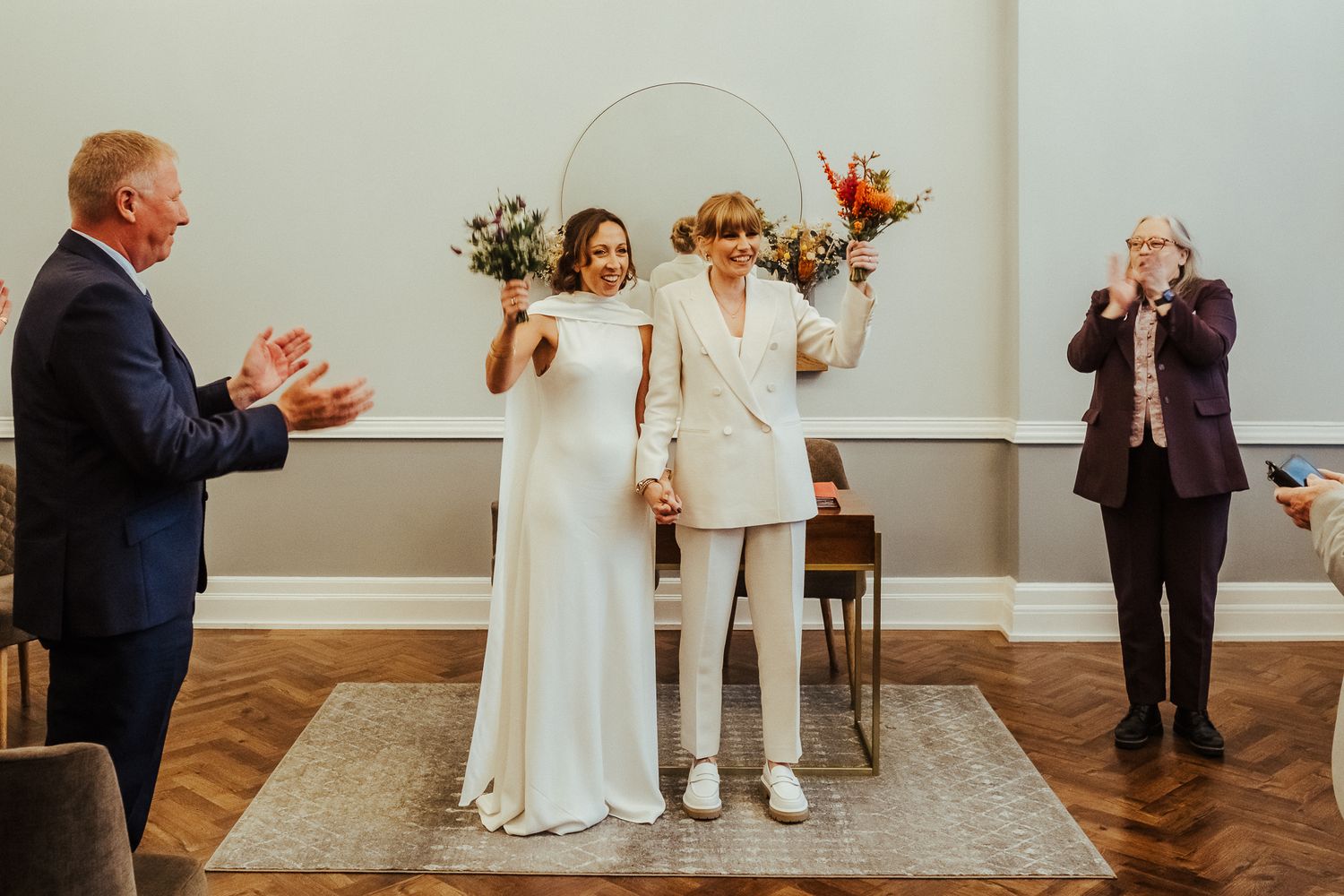 Wedding celebration in bright indoor venue with guests applauding couple in white attire.