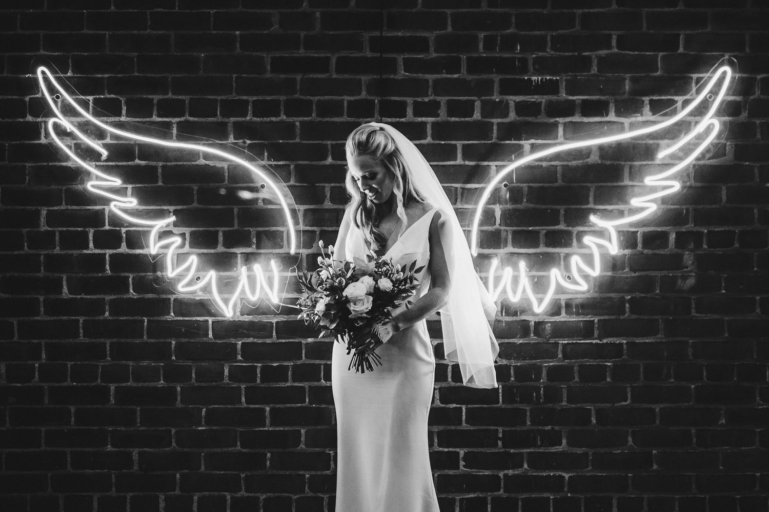 Silhouette against brick wall with illuminated angel wing art installation.
