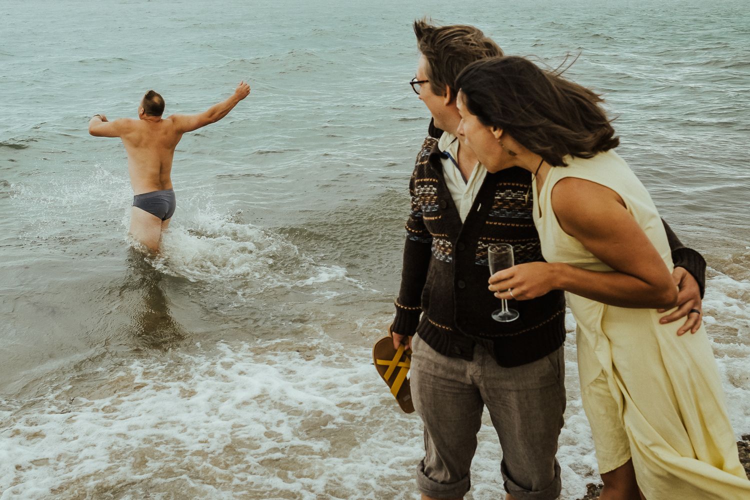 People splashing and playing in ocean waves during sunset celebration.