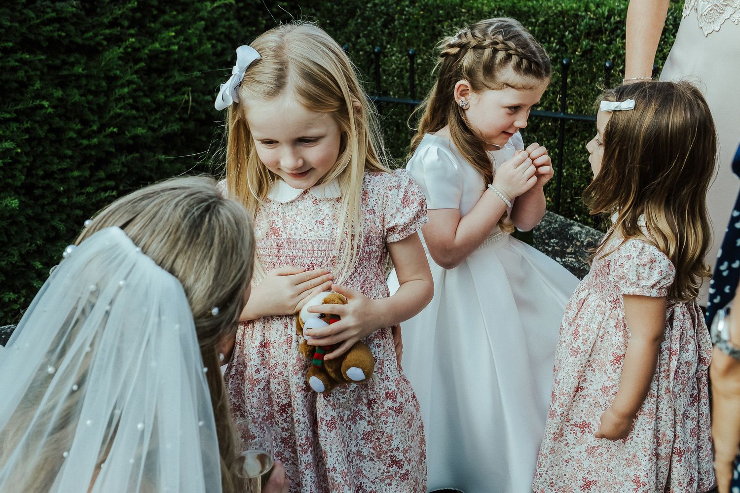 Young flower girls in white and floral dresses gather at outdoor wedding.