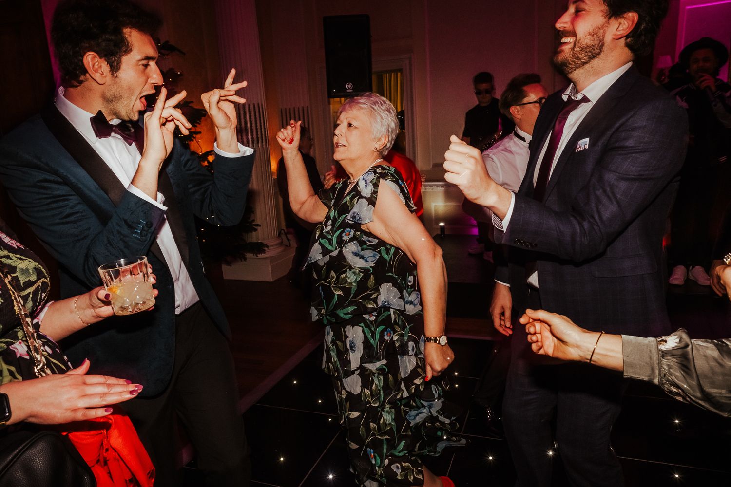 Energetic dancers fill the dance floor at an evening wedding reception with dramatic red lighting.