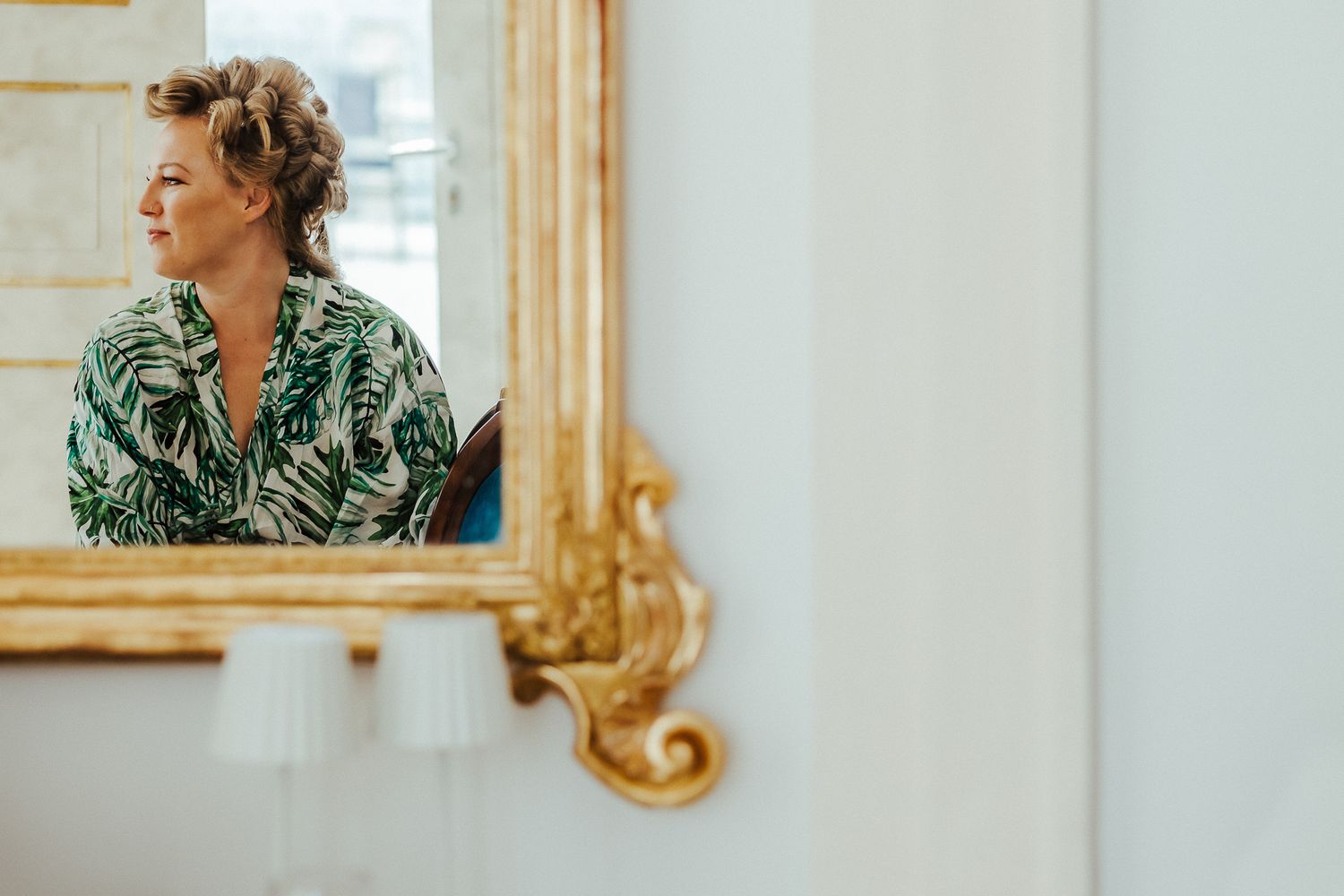 Person in floral print robe poses elegantly beside ornate gold mirror during wedding preparations.