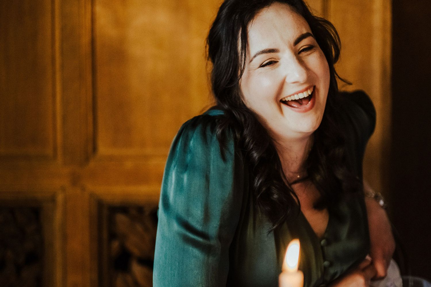 Wedding party sharing laughter and candid moments in venue with warm wooden backdrop.