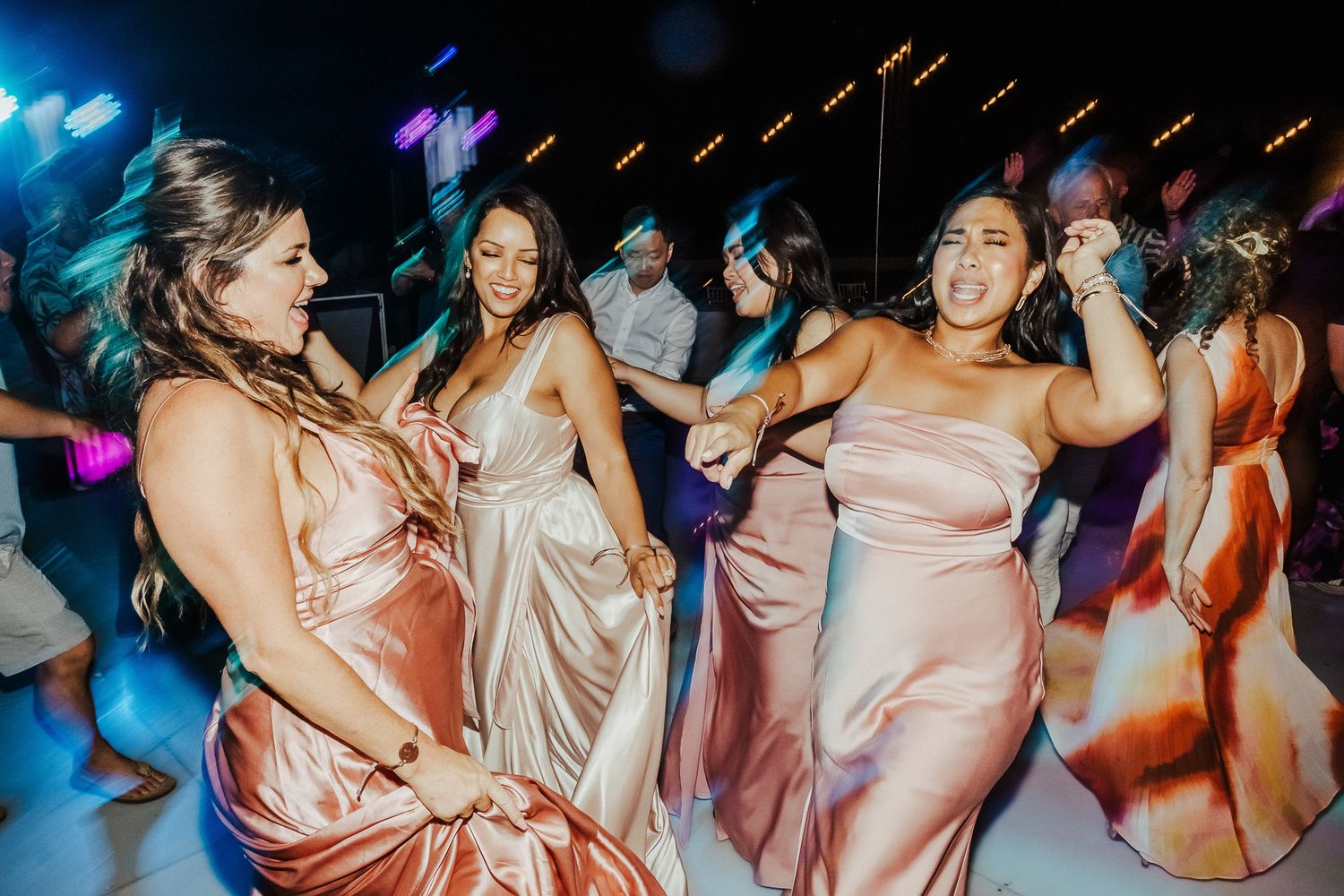 Energetic dance party with guests in pink dresses under blue lighting.