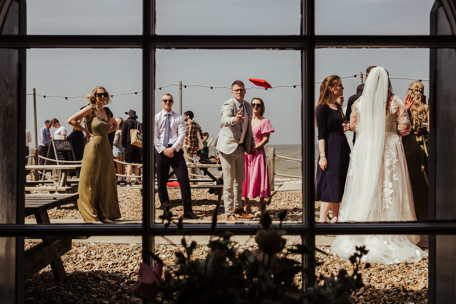 Wedding guests interact with a small child during sunny outdoor reception.