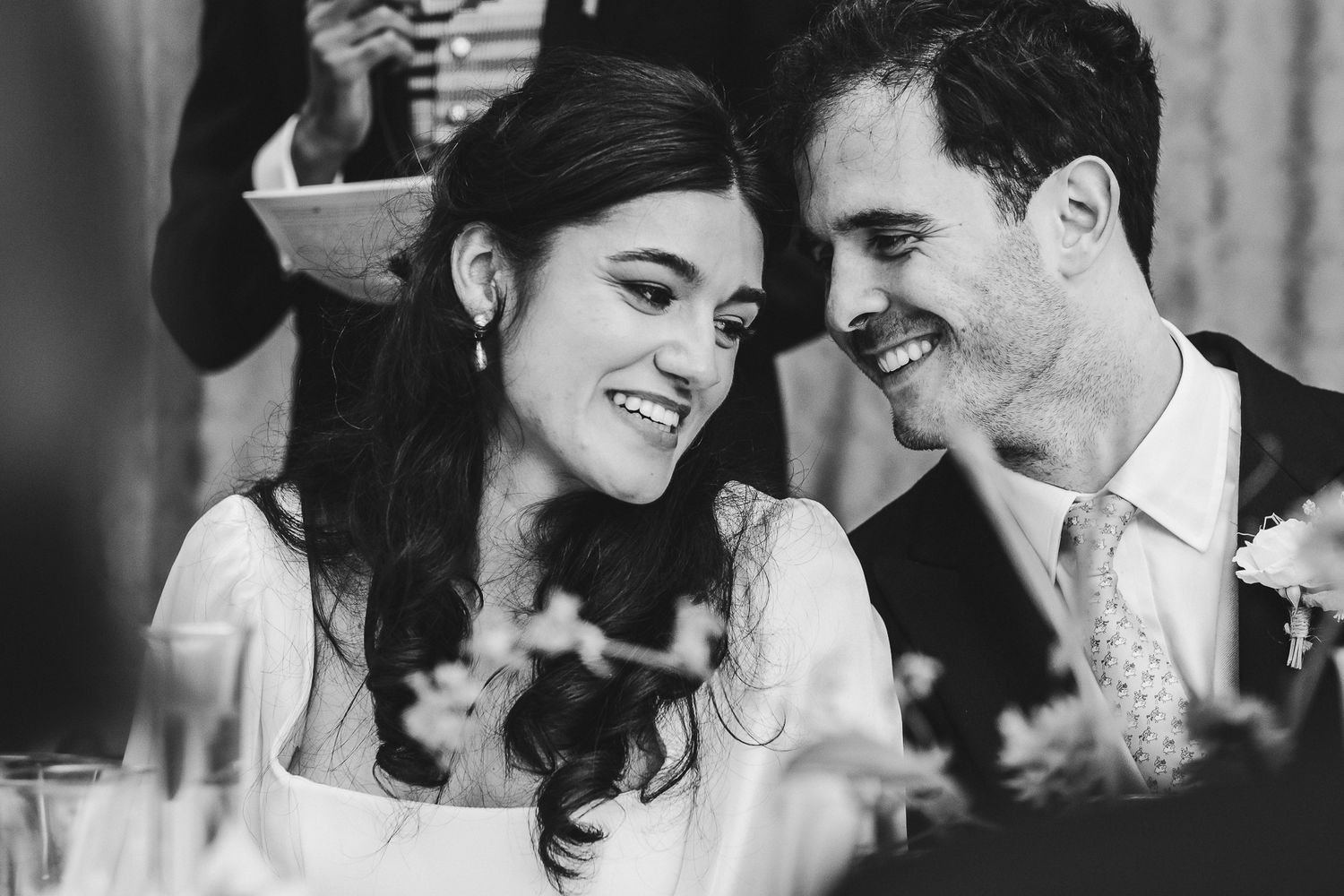Black and white candid photo of couple laughing together at wedding reception.