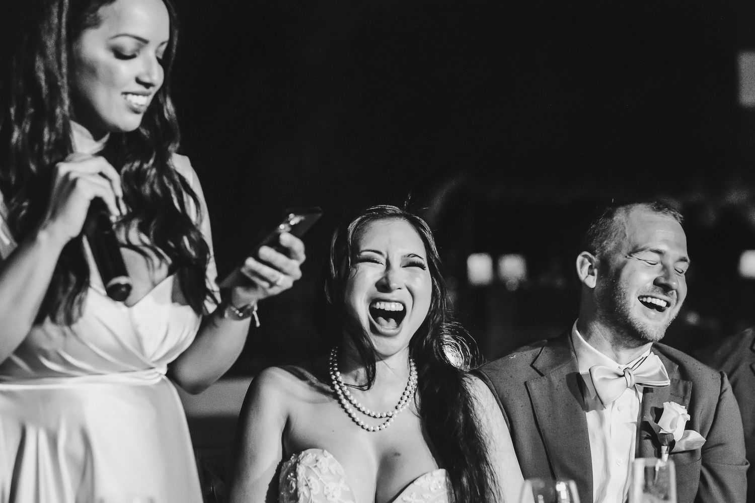 Black and white photo capturing joyful laughter during wedding reception speeches.