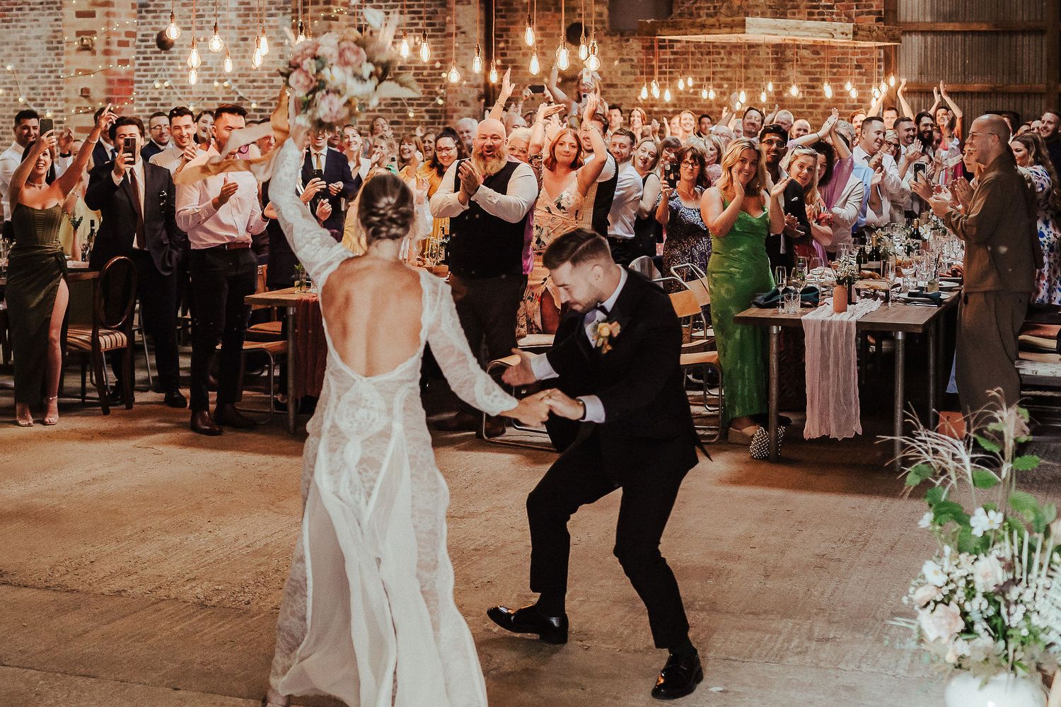 Guests dancing and celebrating at an elegant indoor wedding reception with string lights.
