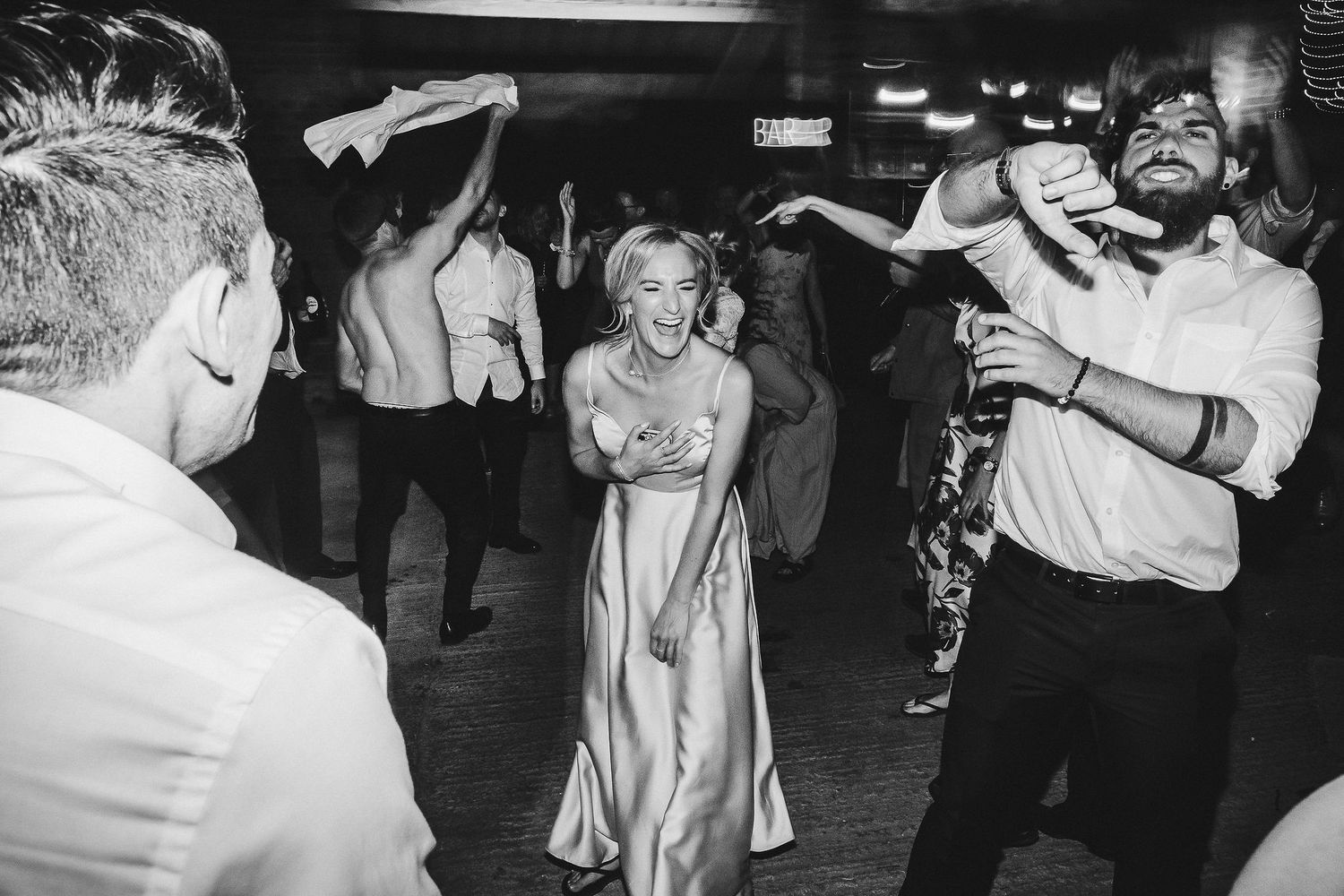 Wedding party members dance enthusiastically at a black and white reception celebration.