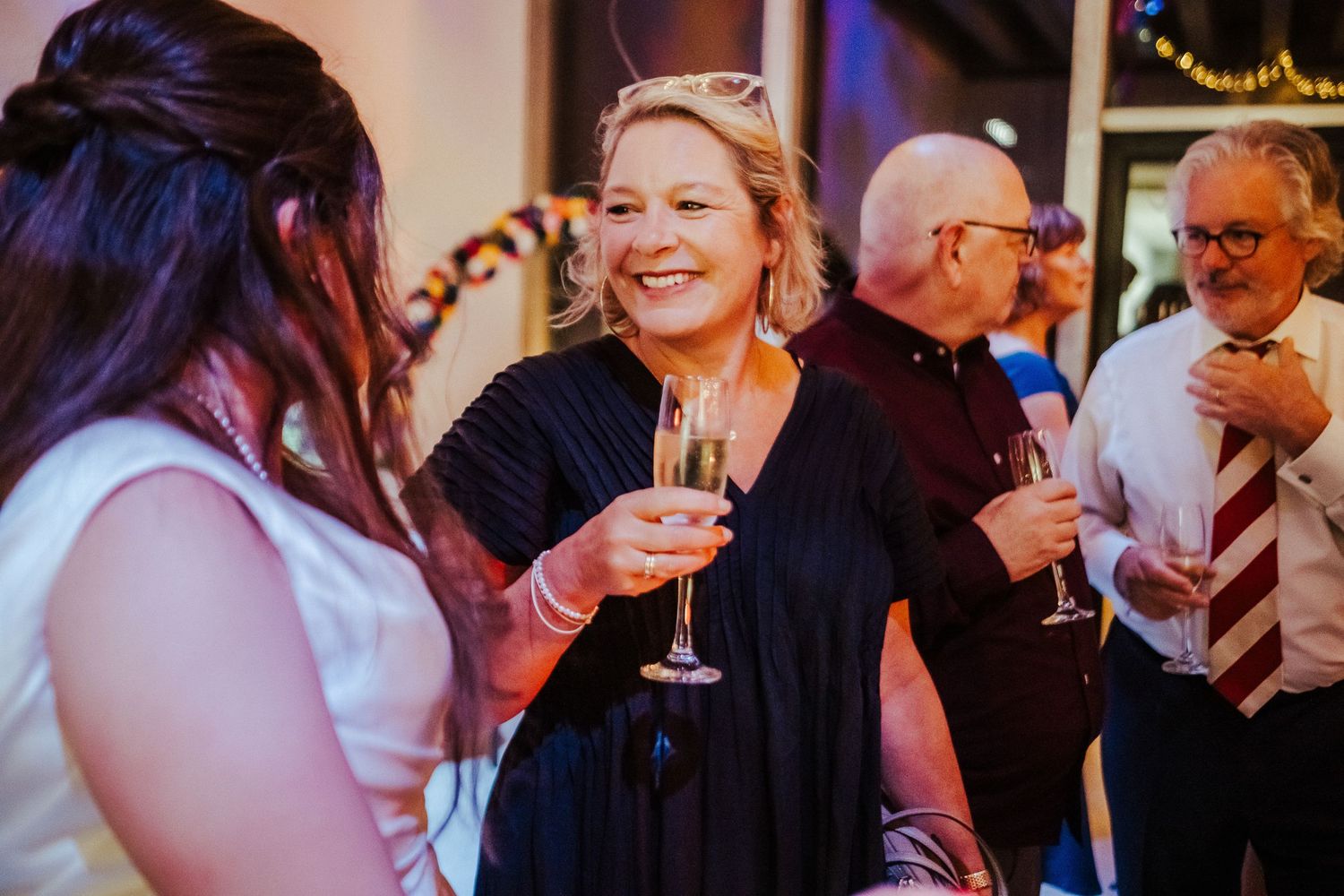Wedding guests share drinks and laughter during evening reception celebration.