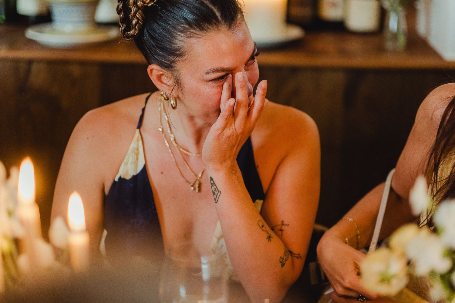 A person in formal attire appears emotional at a candlelit dinner table with decorative floral arrangements.