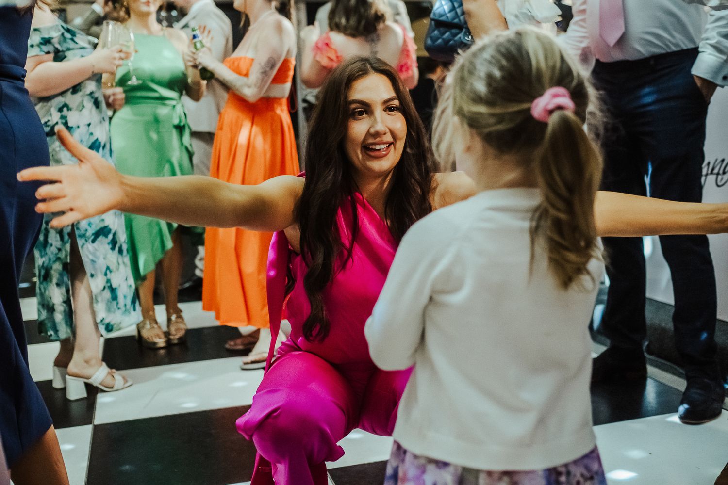 People dancing and celebrating joyfully at a wedding reception with colorful bridesmaids dresses visible in the background.
