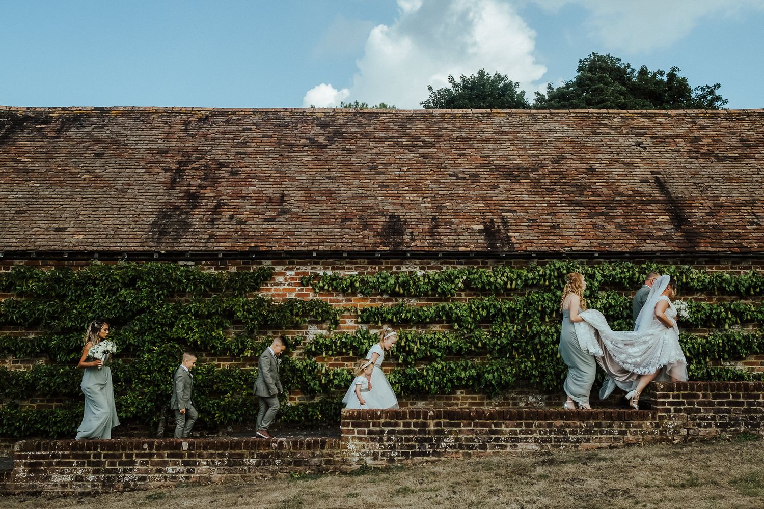 Creative wedding party photo showing group jumping along brick wall in sequence.