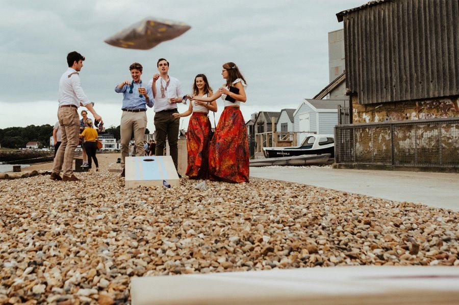 Panoramic view of guests gathered on a pebble beach near a rustic building.