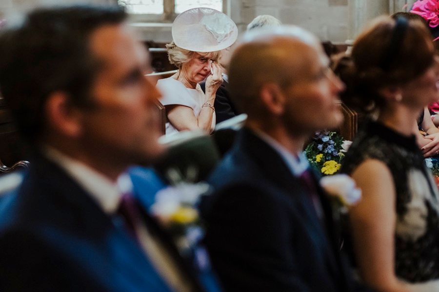 Wedding guests seated in formal attire during an indoor ceremony.