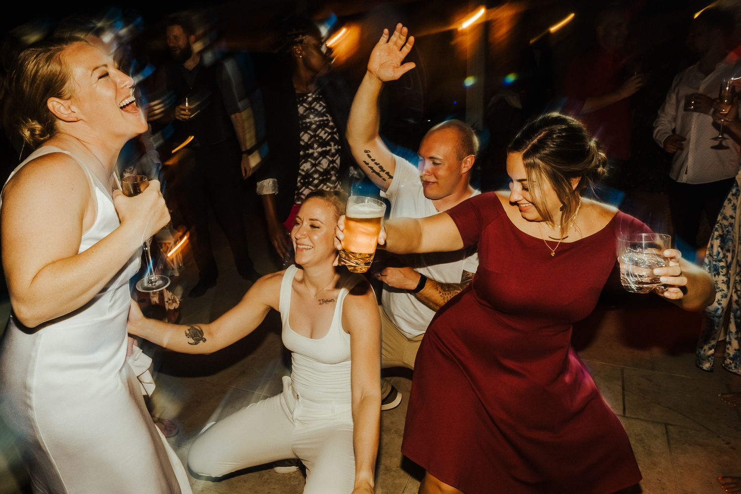 Group of dancers enjoying themselves at a lively celebration with drinks in hand.