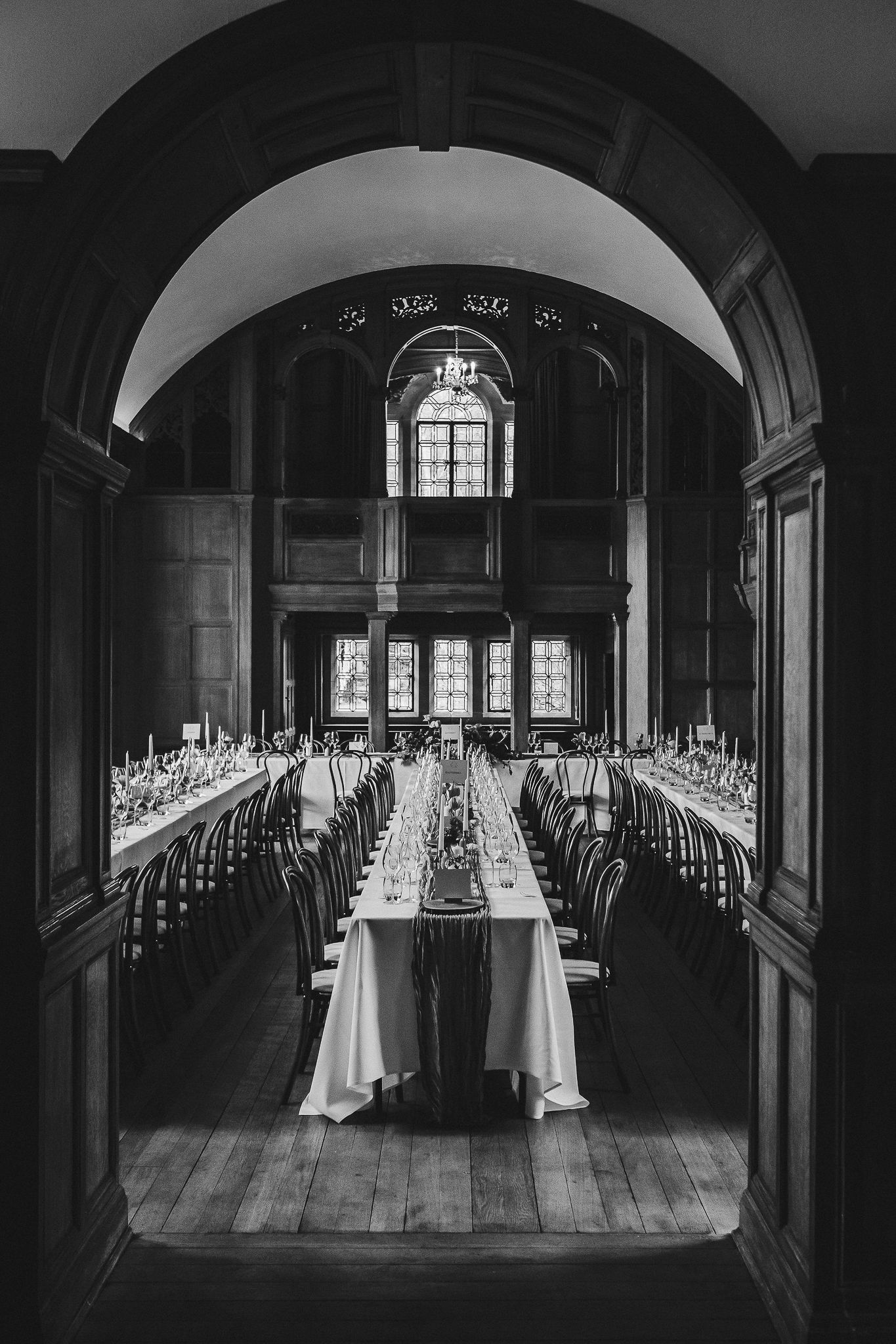 Elegant banquet hall with long tables set for a formal dinner under arched ceilings and stained glass windows.
