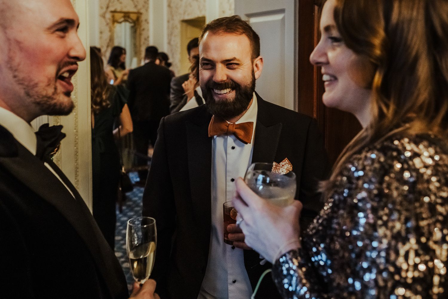 Wedding guests share laughs during reception in formal evening attire.