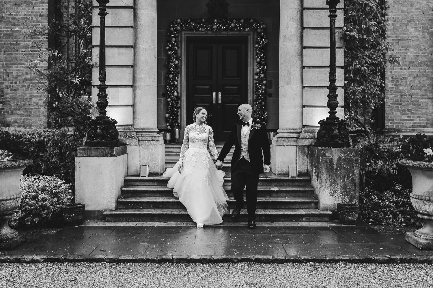 Wedding couple descends stone steps of historic building in rainy weather.