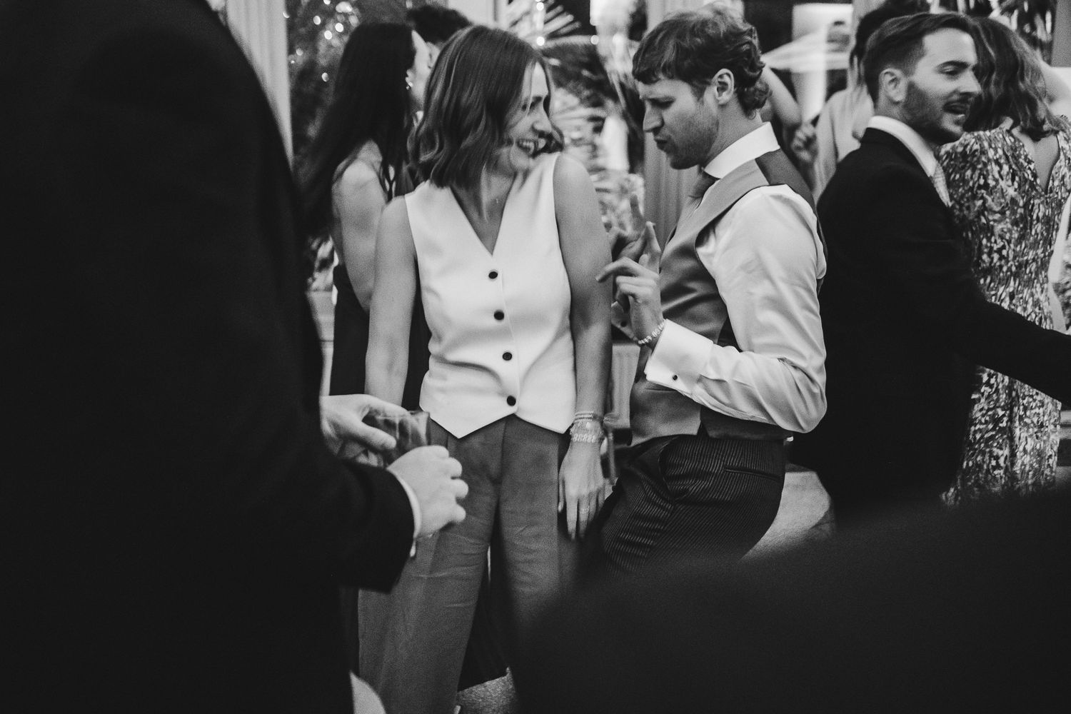 Black and white candid shot of guests in casual attire conversing at a social gathering.
