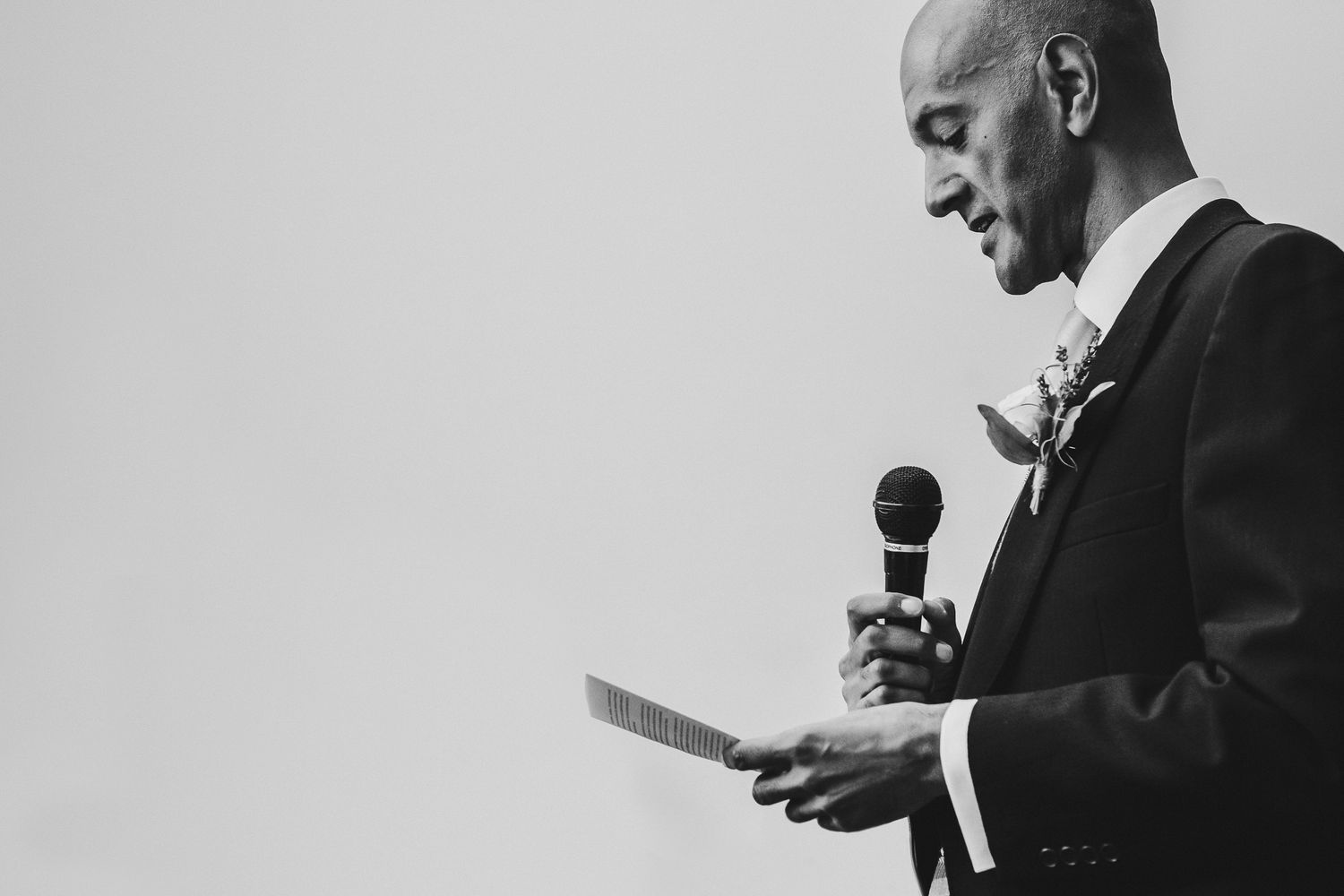 Black and white portrait of speaker giving emotional wedding toast with microphone.