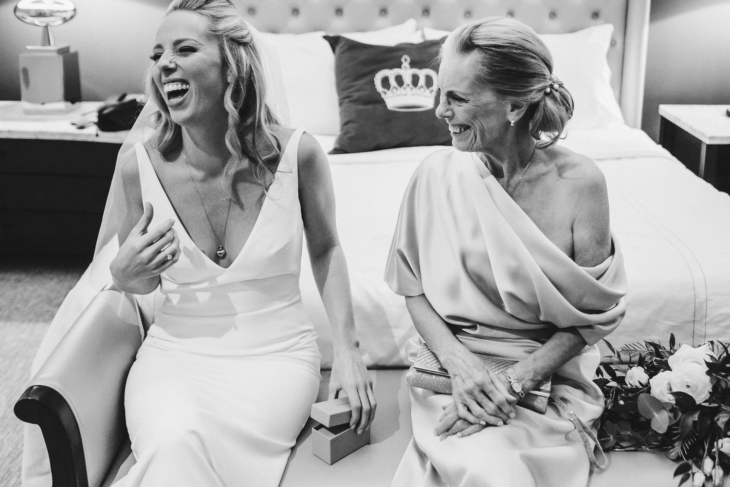 Two women in white dresses sharing a joyful candid moment on a couch.