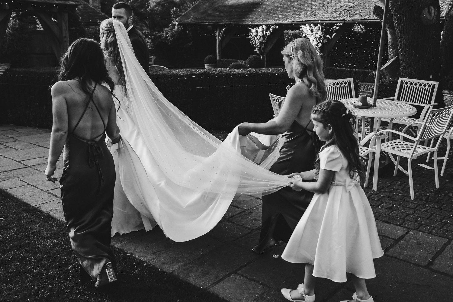Black and white capture of wedding dress train being arranged on stone patio.