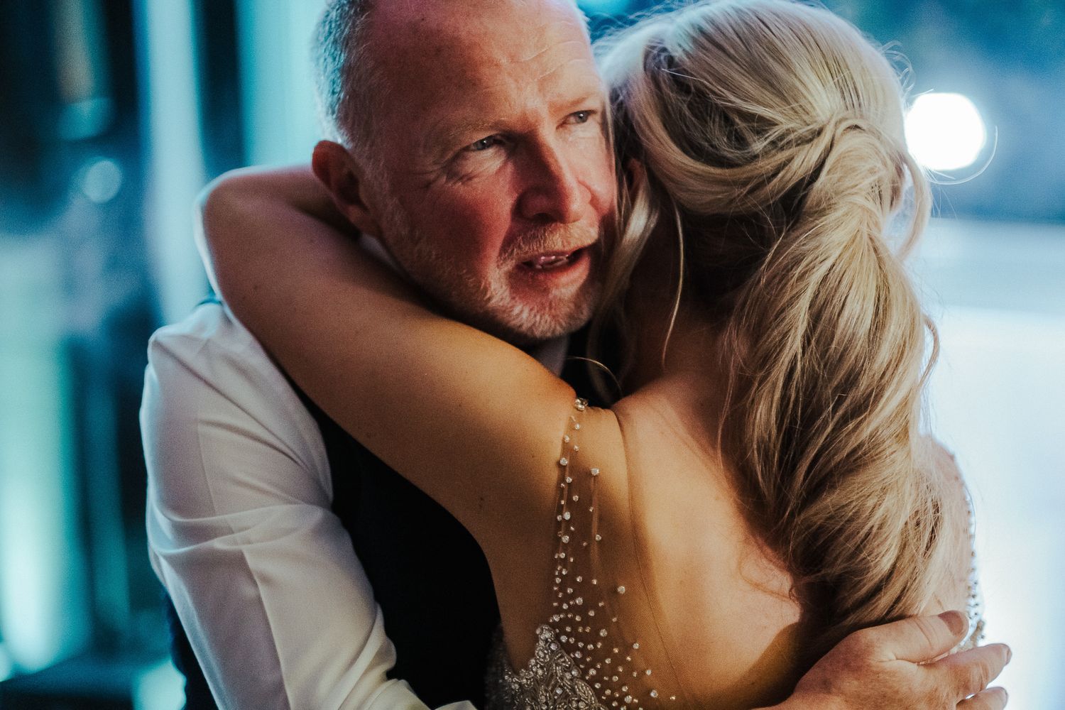 Couple shares an intimate dance moment at an evening wedding reception with dramatic blue lighting.