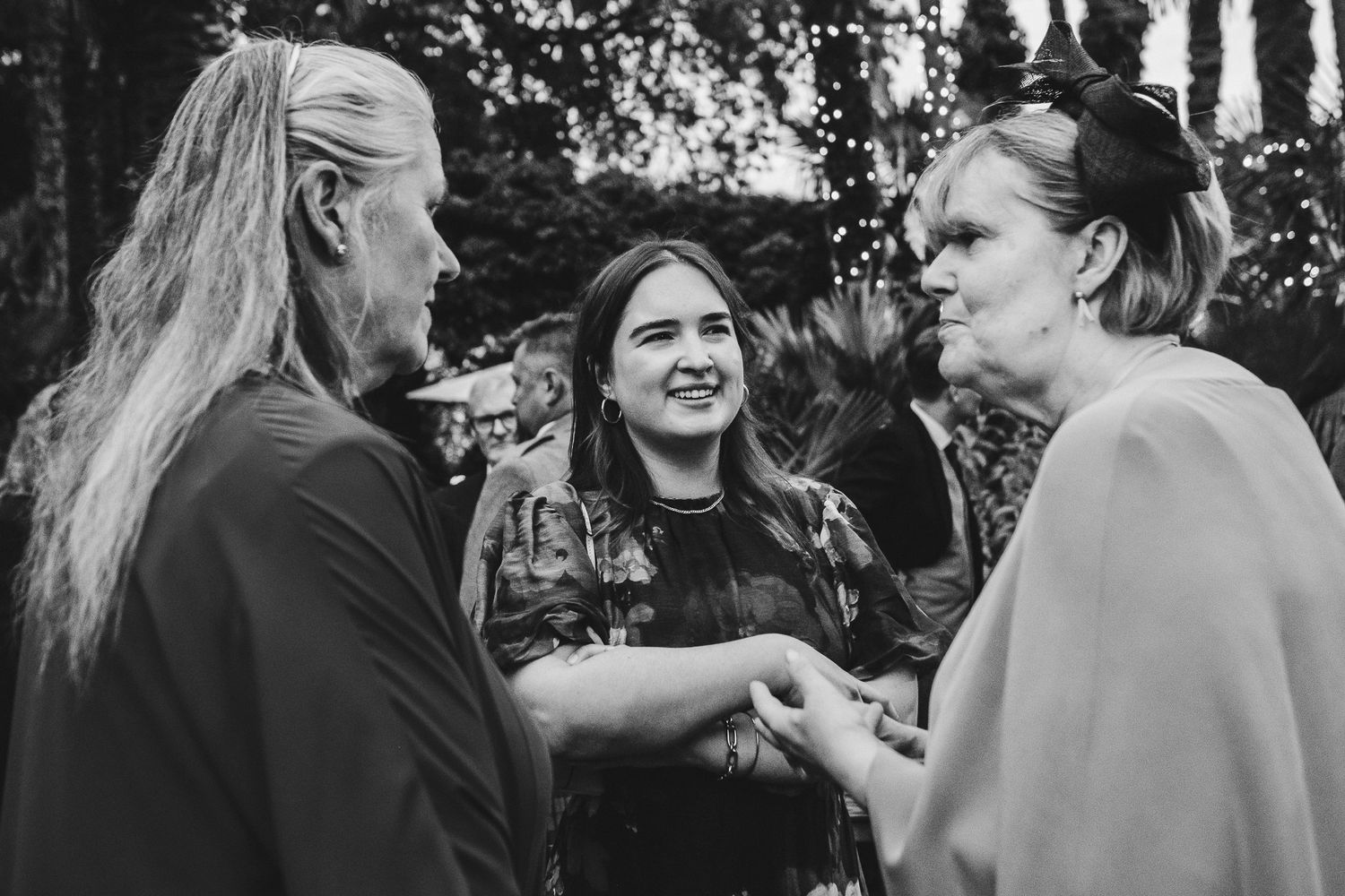 Black and white photo of guests engaged in conversation at an outdoor wedding.
