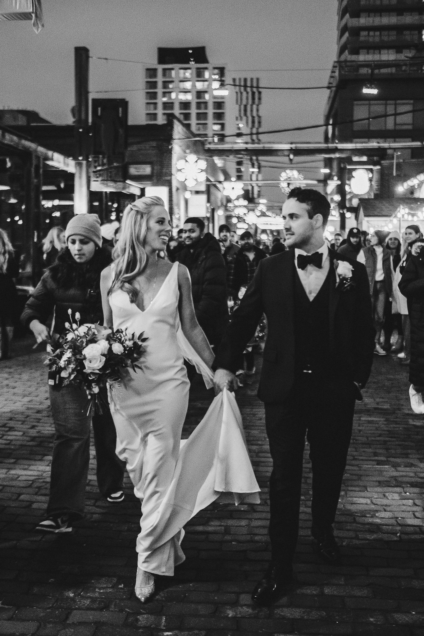 Couple walks through city streets at night holding hands among crowd.